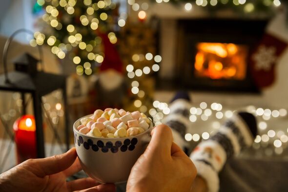 Man enjoying cocoa with marshmallows by warm fireplace with Christmas tree and decorations background.